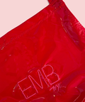 Close-up view of a shiny red apron featuring the embroidered initials 'EMB NYC' on the front.